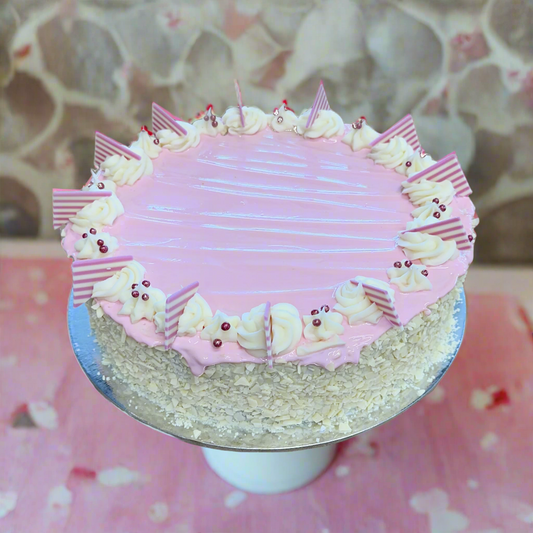 A round mud cake with white and strawberry pink swirls, decorated with strawberry ganache and pink and white chocolate pieces.