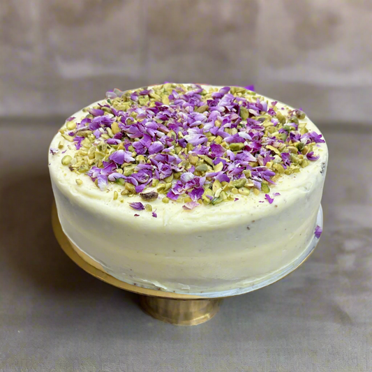 A carrot and orange cake with cream cheese frosting, topped with rose petals and pistachios.